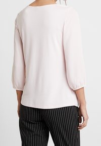 Ljust rosa blus med tre fjärdedels puffärmar. Mjuk tyg med rundad halsringning. Kombinerad med svart och vit randig byxor.