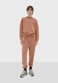 Sweatshirt and sweatpants set in soft, peachy fabric. Features ribbed cuffs and neck, drawstring waist, and small logo detail on the chest.