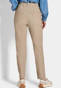 Lichtbeige broek met een aansluitende tailleband, twee achterzakken en taps toelopende pijpen, gecombineerd met lichtgekleurde sneakers.