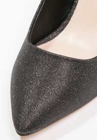 Chaussure à talon haut noire pailletée avec bout pointu et surface texturée, dotée d'un intérieur lisse et d'une silhouette élégante.
