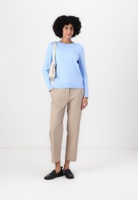 Lyseblå genser med rund hals, kombinert med beige bukser og svarte loafers. Genseren har et lite logo på brystet.