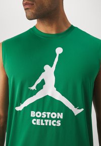 Groen mouwloos shirt met een witte afbeelding van een springend figuur en de tekst "BOSTON CELTICS" in vetgedrukte blokletters eronder.