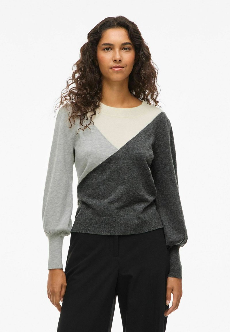 Pull à manches longues avec un design en blocs de couleurs incluant des panneaux gris, gris clair et noir, des poignets côtelés et une coupe décontractée.
