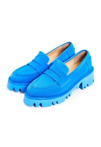 Mocassins en daim bleu vif avec semelles épaisses à rainures et un détail de bride sur le dessus, présentés en angle sur fond blanc.