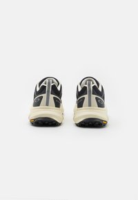Sapatilhas atléticas pretas e bege com um upper texturizado, riscas contrastantes e uma sola robusta. Apresentam um logótipo discreto no calcanhar.