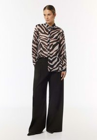 Sheer, long-sleeve blouse with a zebra print pattern in black and beige. Features a pointed collar and button-down front, paired with black wide-leg trousers.