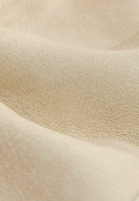 Beige stof met een zachte, gestructureerde oppervlakte, gekenmerkt door zachte golven en een lichte glans. Materiaal lijkt weelderig en glad.