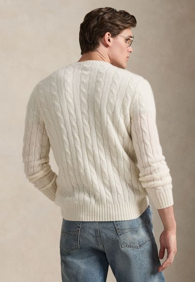 Camisola creme de malha canelada com corte descontraído, apresentando punhos e bainha canelados. Usada com jeans azul claro, destacando a textura e o padrão.