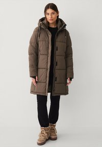 Brun puffjakke med hætte, med kviltede sektioner, frontlynlås og justerbare snore. Båret over sort tøj og støvler.