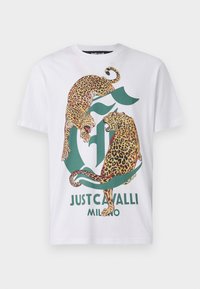 Biała koszulka bawełniana z zielonym logo przedstawiającym dwa lamparty w stylu graficznym. Pod logo znajduje się tekst "Just Cavalli Milano" napisany pogrubioną czcionką.