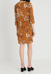 Hnědé květované šaty s tříčtvrtečními rukávy a zadním zipem. Obsahují bílé a fialové květinové vzory na texturovaném pozadí.