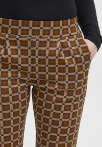 Ruskeat ja keltaiset ruudulliset housut, joissa on teksturoitu kangas, sivutaskut ja slim fit -malli.