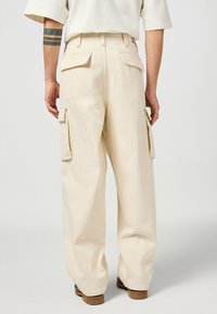 Beige cargo broek met grote zijzakken, een losse pasvorm en stevige stof. Inclusief zichtbare stiksels en een merketiket.
