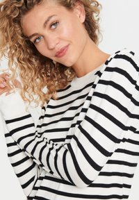 Pull rayé noir et blanc avec un col rond, des poignets côtelés et une coupe décontractée. Le tissu semble doux et tricoté.
