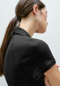 Black short-sleeve polo shirt with a soft texture. Features a fitted design and a slightly structured collar. Silver drop earrings with beads.