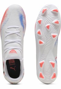 Chaussures de sport blanches avec des accents texturés bleus et roses, dotées d'un design à lacets et d'une semelle en caoutchouc à motifs avec des crampons roses.