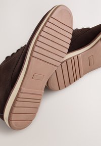Braune Velourslederschuhe mit Gummisohlen. Die Außensohle verfügt über horizontale Rillen für besseren Halt, mit einer cremefarbenen Zwischensohle und dezenten Strukturdetails.