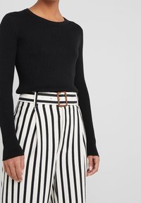 Haut noir à manches longues côtelé associé à un pantalon taille haute blanc à rayures noires, avec une large ceinture marron à boucle.