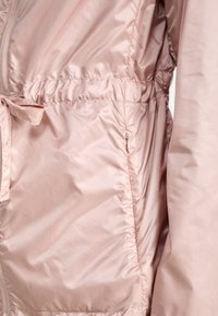 Chaqueta acolchada de color rosa claro con cremallera y cintura ajustable, con tejido suave y brillante y puños elásticos. Decorada con un detalle de lazo.
