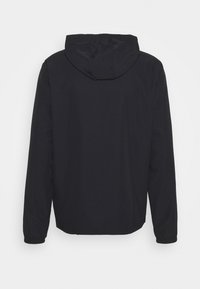 Veste légère noire à capuche avec manches longues et poignets élastiques, montrée de dos sur un fond blanc uni.