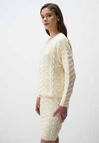 Set di maglione e gonna a maglia crema con motivi testurizzati, tra cui trecce e pois, caratterizzato da una vestibilità morbida e un tessuto soffice e peloso.