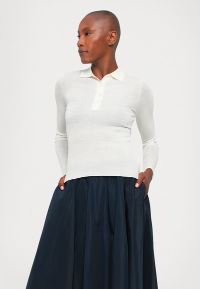 Bílý dlouhý rukáv polo top s texturovaným pleteným materiálem a třemi knoflíky vpředu, spárovaný s tmavou, objemnou sukní.