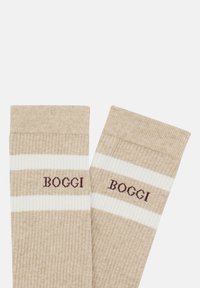 Calcetines beige con textura acanalada que presentan rayas blancas y un logo en color burdeos que dice "BOGGI". Suave al tacto y de diseño hasta el tobillo, ideales para uso casual.