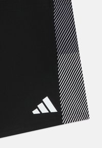 Shorts de sport noirs avec un logo à trois bandes blanches et un motif rayé vertical noir et blanc contrasté sur un côté.