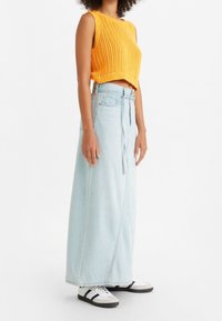 Top corto all'uncinetto di colore arancione abbinato a una gonna maxi in denim blu chiaro con cintura in vita. Sneakers bianche e nere completano l'outfit.
