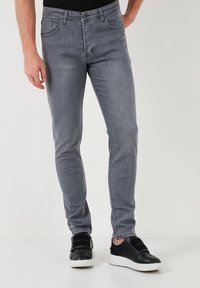 Vaqueros grises de corte ajustado, hechos de denim, con cinco bolsillos y un sutil acabado desgastado. Combinados con zapatillas negras tipo slip-on.