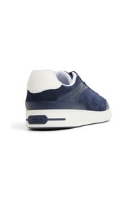 Zapatillas de ante azul marino con acentos blancos y suela de goma, que presentan una textura suave, punta redonda y un sutil detalle de logotipo en el talón.