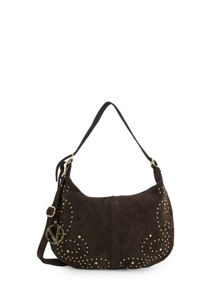 Sac à bandoulière en daim brun foncé avec motifs en spirale de clous dorés, sangle ajustable et un pendentif rond avec logo en or suspendu sur le côté.