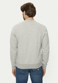 Sudadera gris claro con mangas largas, cuello redondo y puños acanalados. Textura suave, diseño simple, combinada con vaqueros azules.