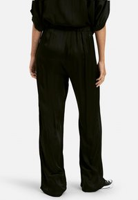 Pantalones de satén negro con una textura suave, que cuentan con una cinturilla elástica y un diseño de pierna ancha, mostrados desde la parte de atrás con un brillo sutil.