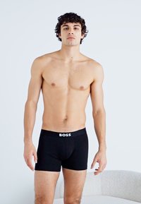 Boxers noirs avec une coupe ajustée et une ceinture élastique arborant le logo "BOSS" en blanc. Tissu lisse avec un design classique.