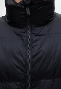 Gros plan sur le col et la fermeture éclair entièrement fermés d'une doudoune noire sur la partie supérieure de la poitrine d'une personne.