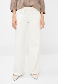 Pantalons larges blancs avec une taille à cordon, en tissu lisse, et poches latérales. Associés à des escarpins beiges à bout pointu.