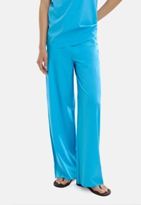 Jasnoniebieskie szerokie spodnie wykonane z gładkiego, lekkiego materiału, w połączeniu z klapkami, charakteryzujące się luźnym krojem i bocznymi kieszeniami.