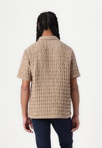 Beige kortærmet skjorte med en struktureret, mønstret overflade. Har en standard krave og lige kant, lavet af et letvægtsstof.