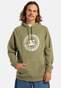 Felpa verde oliva con tasca a marsupio frontale, caratterizzata da un logo grafico bianco circolare al centro e polsini a coste.
