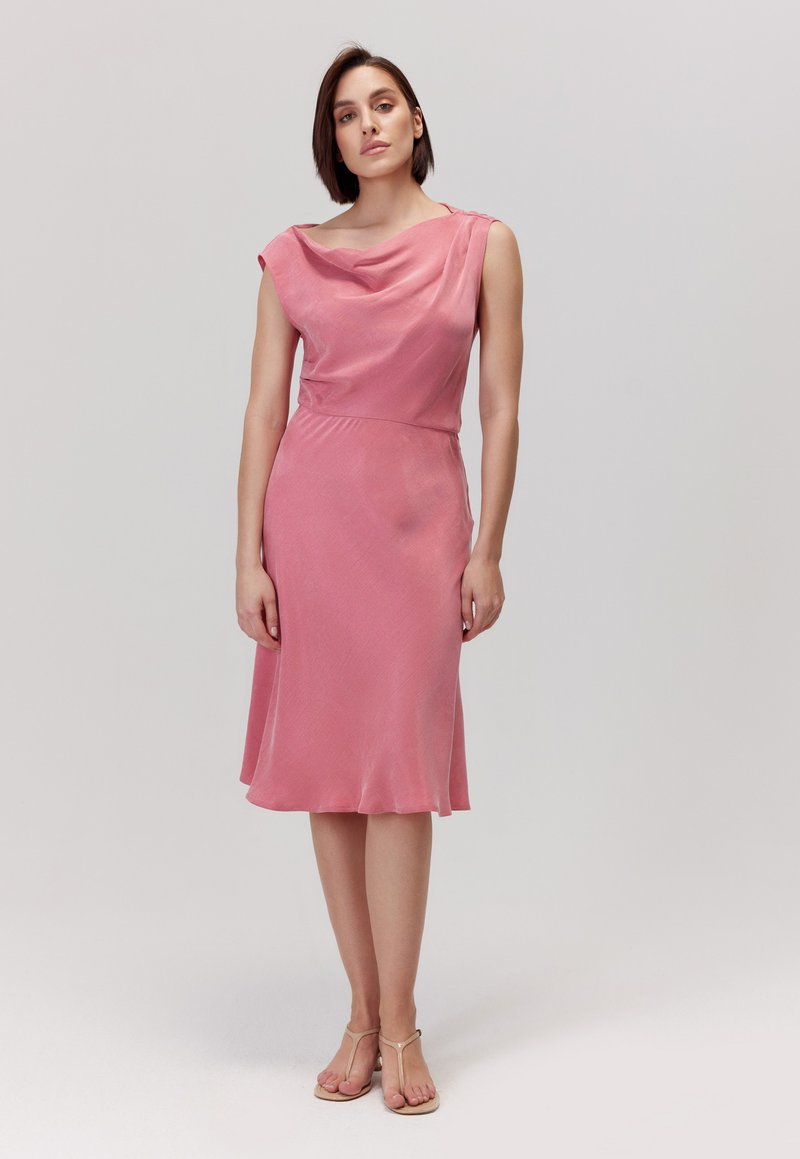 Różowa sukienka z dekoltem typu cowl, krótkimi rękawami i sylwetką w linii A. Gładki materiał z delikatnym połyskiem, długość do kolan. Podkreślona talia.