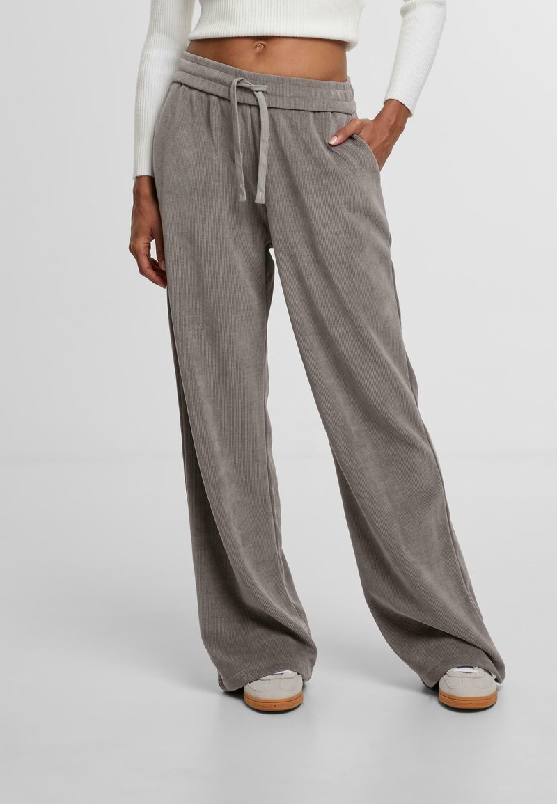 Grijze corduroy wijde broek met een trekkoord in de taille, zijzakken, rustend op een model die lichte sneakers draagt. Soepele, textuurrijke stof.