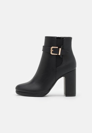 Bottines noires en cuir lisse avec un bout carré, un talon épais haut et une boucle dorée décorative sur le côté.