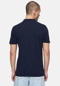 Polo shirt navy con maniche corte, colletto rigido e aperture laterali, realizzato in un morbido tessuto misto cotone. La vista posteriore mostra una texture e una vestibilità lisce.