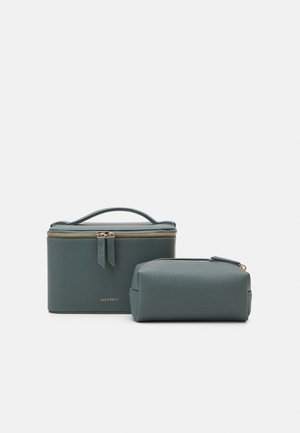Duas bolsas de cosmetológicos de textura suave, em tons de teal, nas formas retangular e cilíndrica, com fechos de correr dourados e uma gravação da marca.