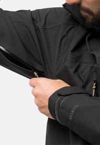 Schwarze wasserdichte Jacke mit strukturierter Oberfläche. Verfügt über einen Reißverschluss an der Seite und einen Klettverschluss an den Ärmeln für eine verstellbare Passform.