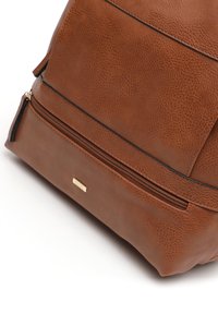 Brown textured leather backpack featuring a zippered pocket, smooth edges, and a small gold hardware accent on the front.