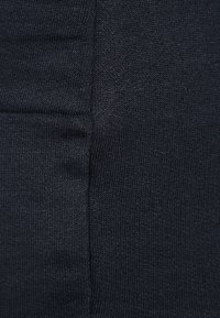 Svart stretchtyg, närbild som visar den släta texturen och den åtsittande passformen med minimala sömmar och inga synliga mönster eller utsmyckningar.