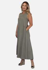 Bezramienna, długa, jasnoszara sukienka uszyta z materiału o gładkiej fakturze. Posiada wysoki dekolt, boczne kieszenie oraz delikatne złote akcenty.
