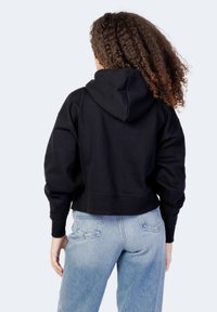 Czarna skrócona bluza z kapturem, o miękkiej fakturze i ściągaczach przy rękawach, w połączeniu z jasnoniebieskimi dżinsami o wysokim stanie.